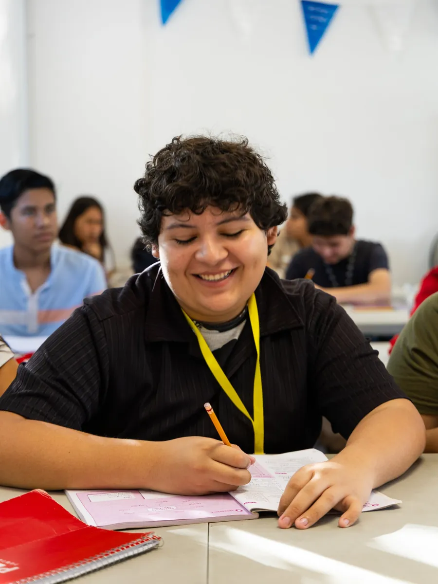 Estudiante sonriente escribiendo en su cuaderno durante una clase en PEACE Punta de Mita
